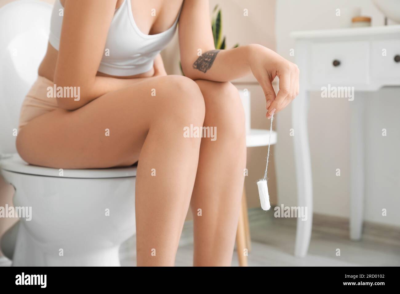 Young woman with tampon sitting on toilet bowl in bathroom, closeup Stock Photo