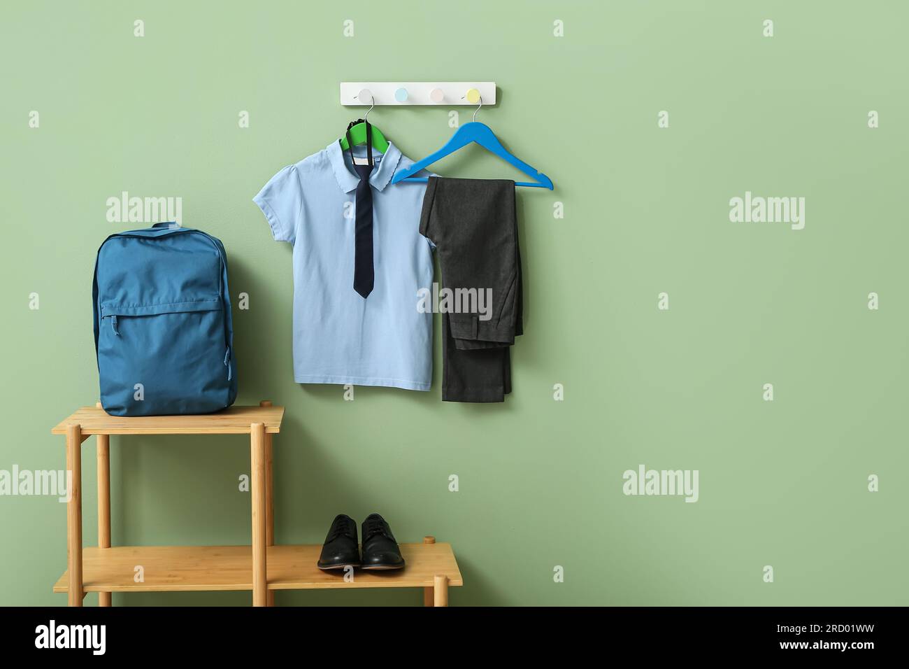 Stylish school uniform hanging on rack with backpack against green wall