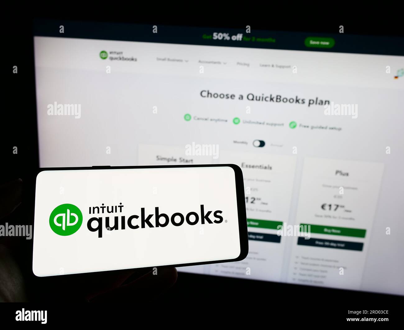 Person holding cellphone with logo of accounting software QuickBooks on screen in front of business webpage. Focus on phone display. Stock Photo