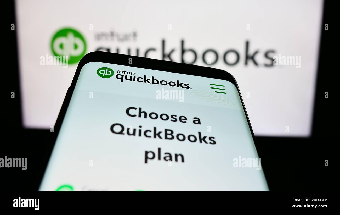 Smartphone with website of accounting software QuickBooks on screen in front of business logo. Focus on top-left of phone display. Stock Photo
