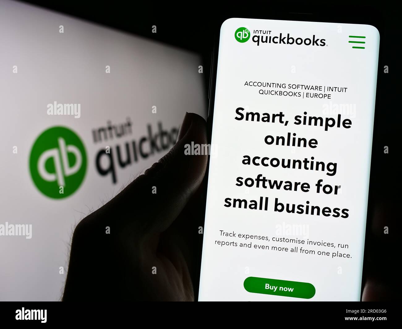 Person holding cellphone with webpage of accounting software QuickBooks on screen in front of logo. Focus on center of phone display. Stock Photo