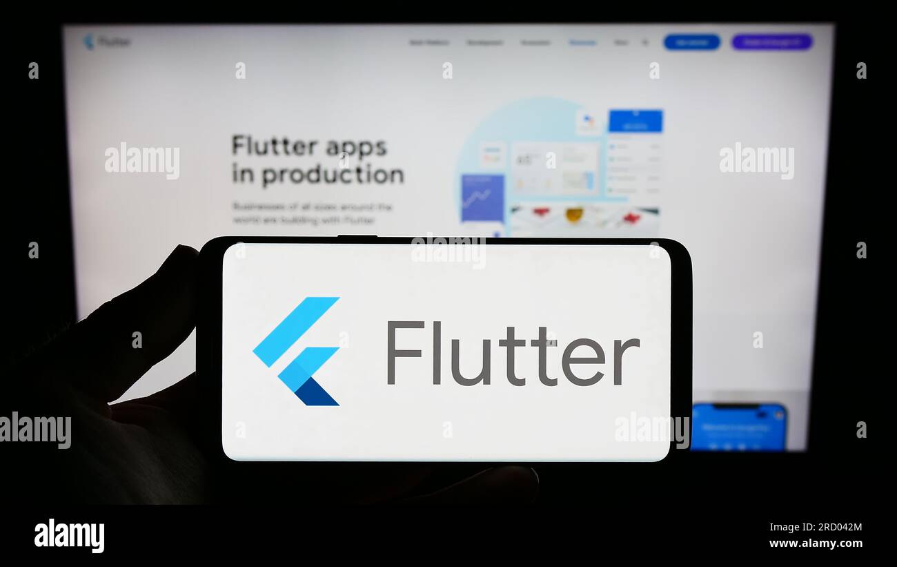 Person holding smartphone with logo of UI software development kit Flutter (Google) on screen in front of website. Focus on phone display. Stock Photo