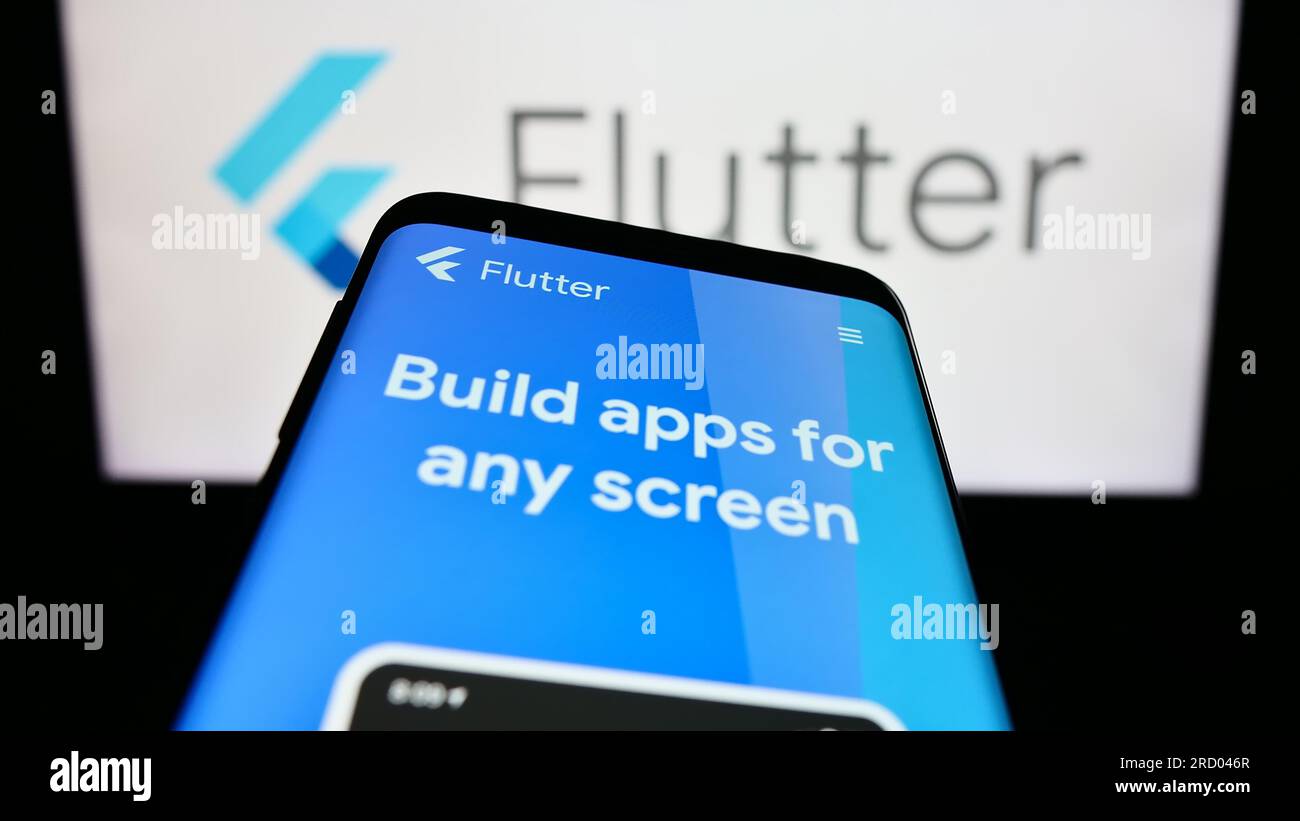 Smartphone with webpage of UI software development kit Flutter (Google) on screen in front of logo. Focus on top-left of phone display. Stock Photo