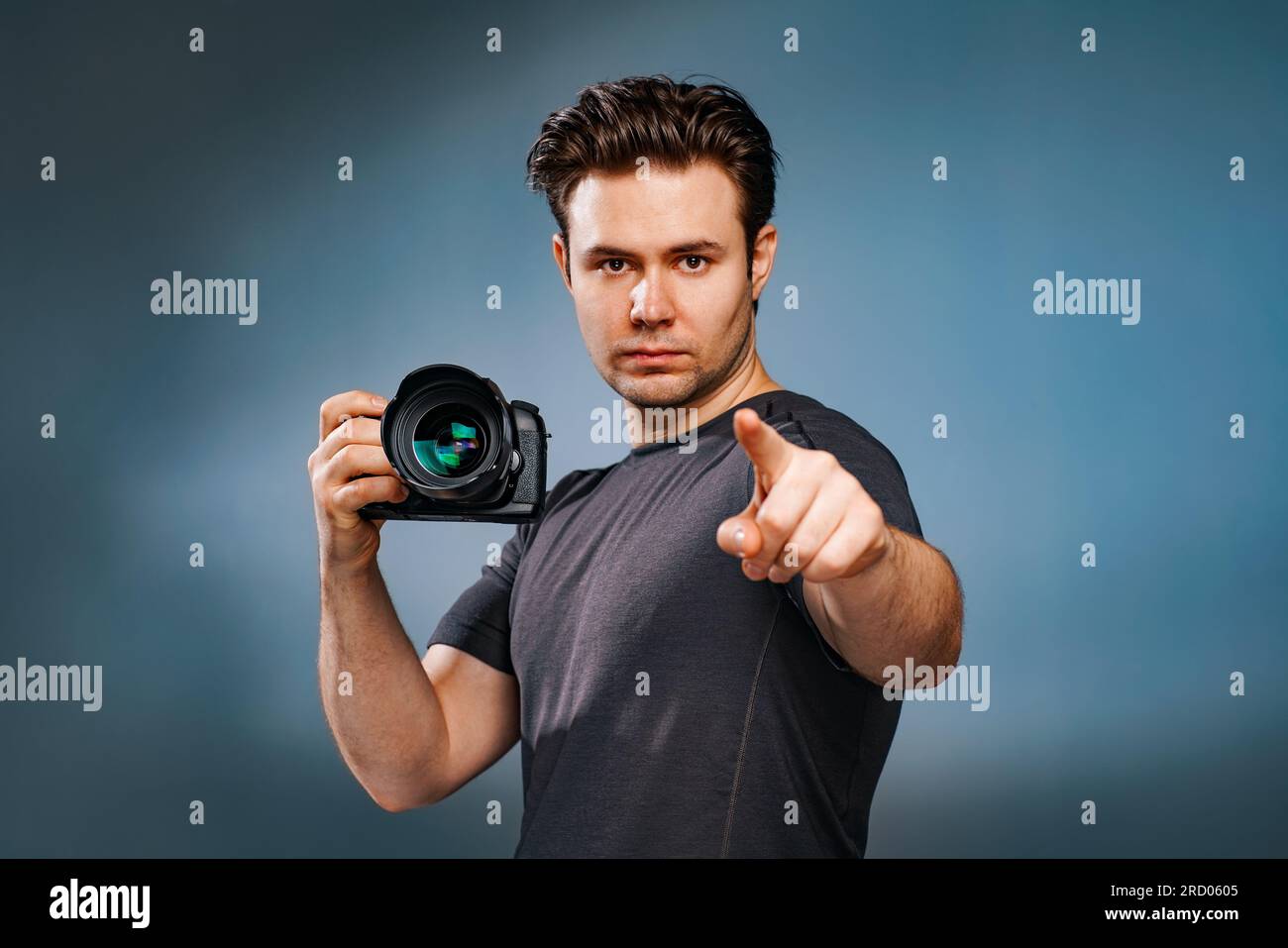 Young brunette man pointing with finger and holding camera in hand Stock Photo