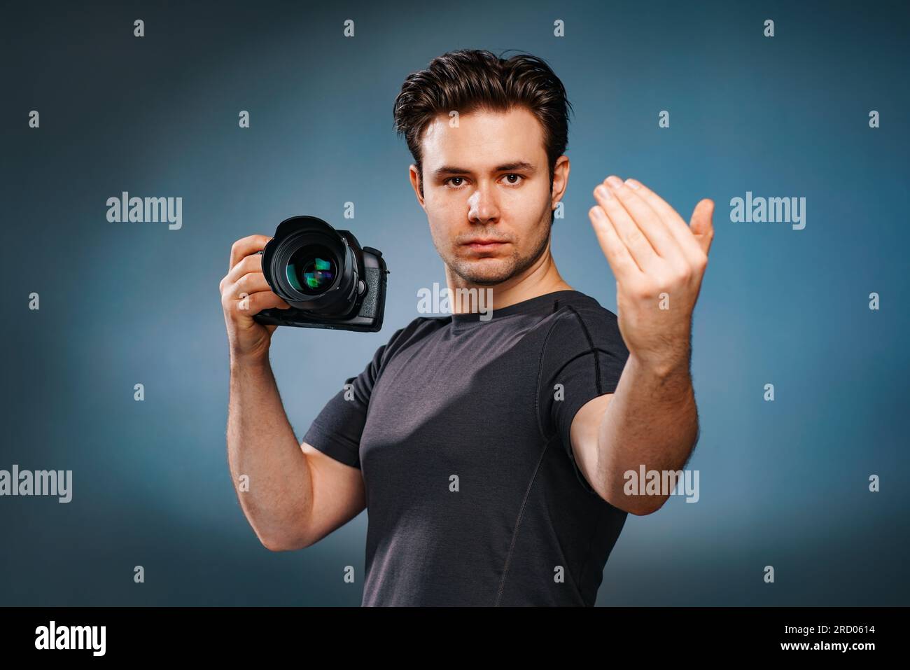 Young brunette man calling handsign and holding camera in hand Stock Photo