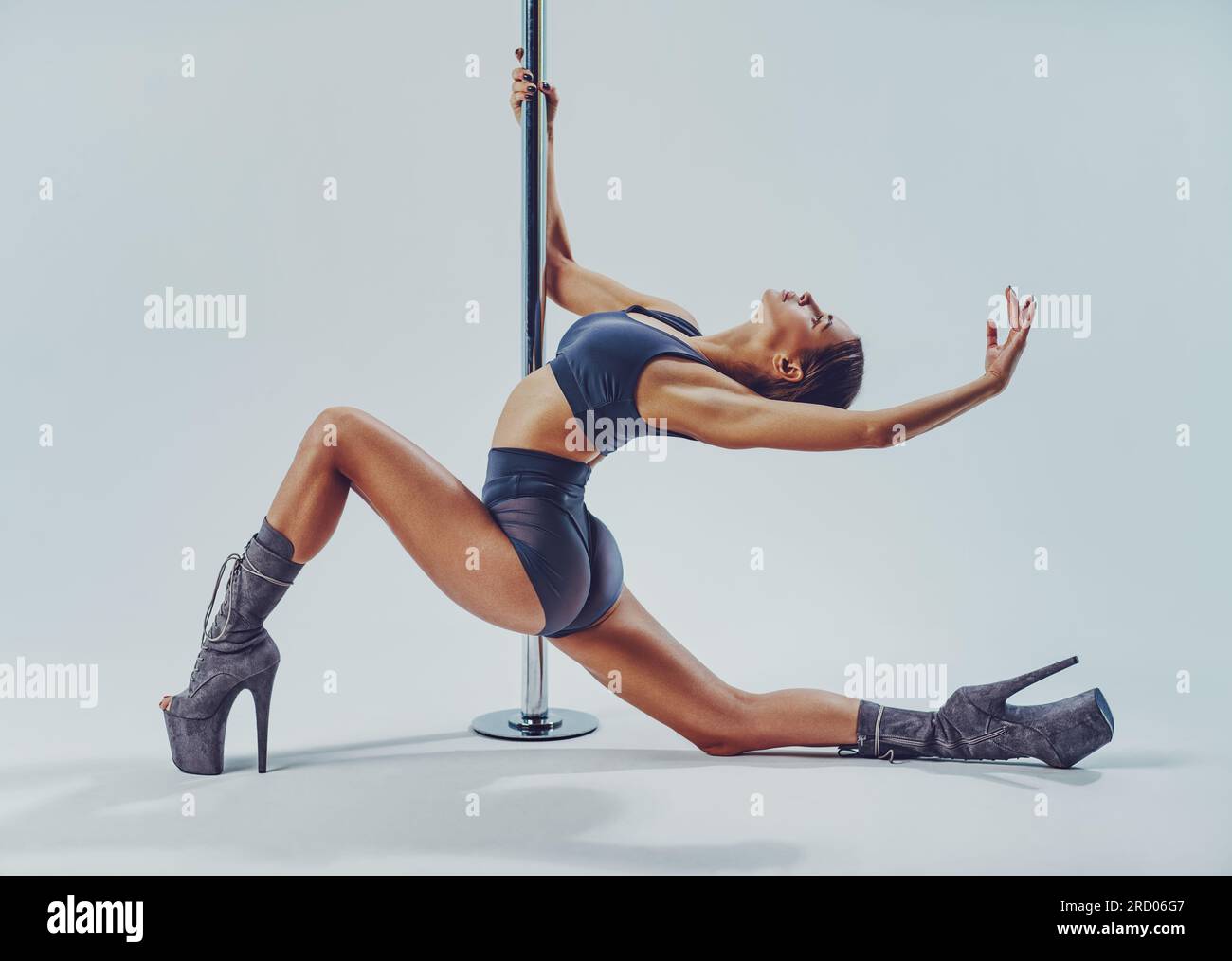 Young slim woman pole dancing on white wall background Stock Photo