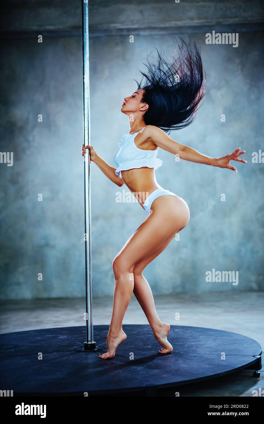 Young slim woman pole dancing on gray wall background Stock Photo