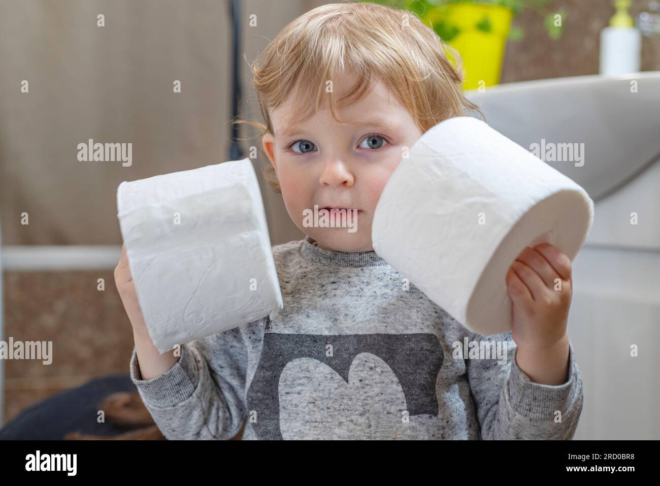 A cute boy is holding toilet paper roll in bathroom. Young boy with
