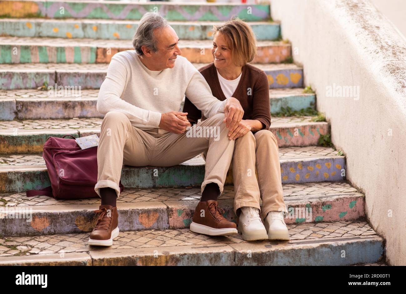 Mature Man And Woman With Backpack Sitting On Steps Outdoors Stock Photo