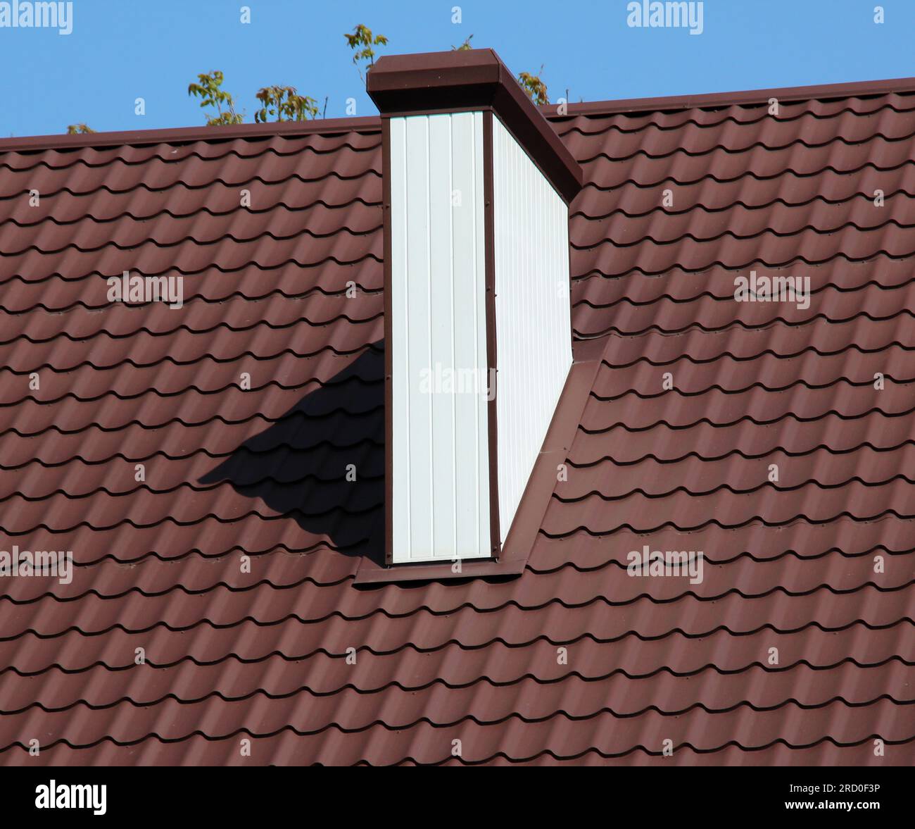 A chimney on the roof of a house covered with metal tiles or a metal