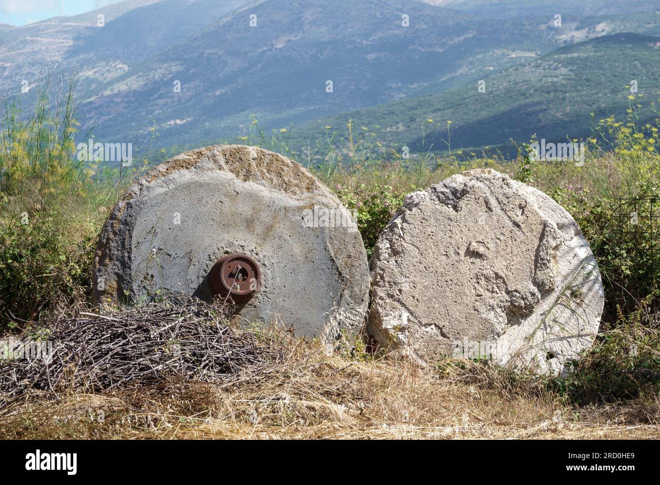 Two redundant olive press grind stones in a field with mountains in the background Stock Photo