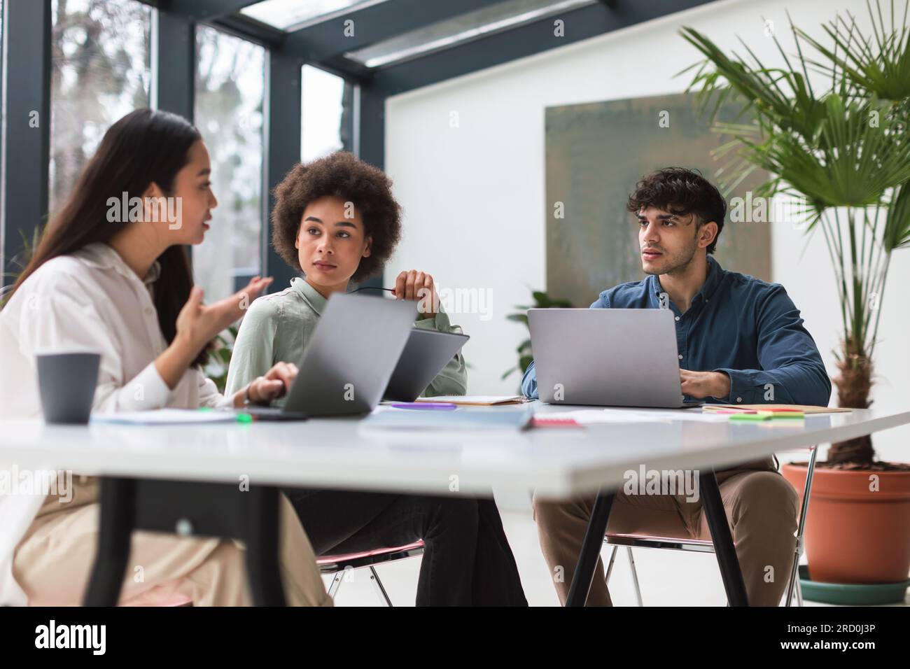 Three young diverse colleagues at laptops bringing ideas at office ...