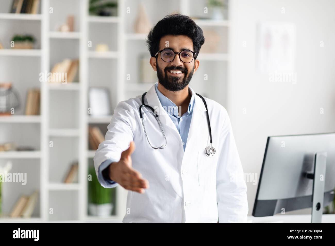 Friendly handsome middle eastern doctor outstretching hand and smiling Stock Photo
