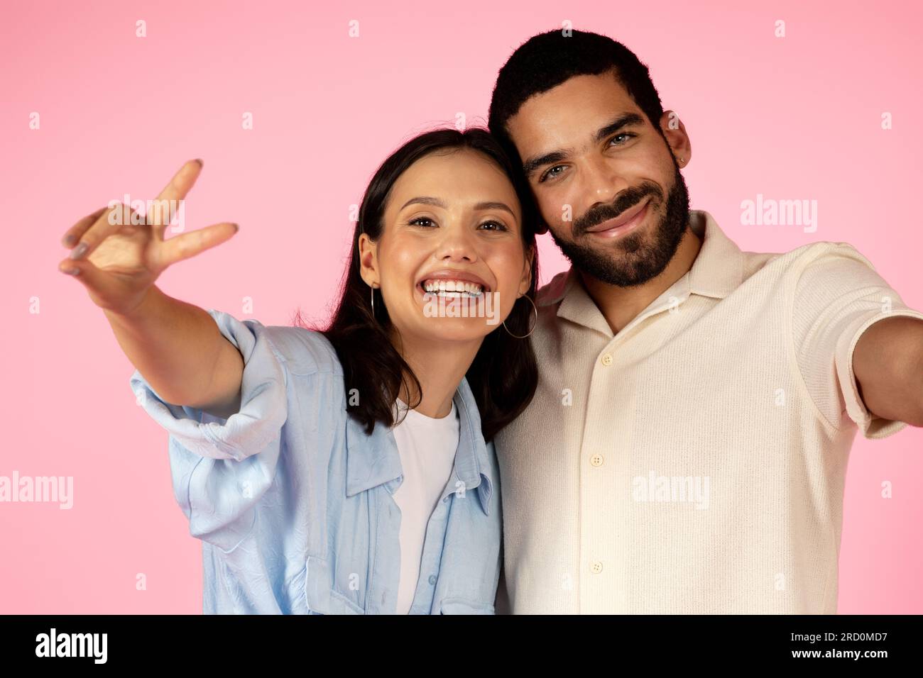 Beautiful cute multiracial young couple taking selfie on pink background Stock Photo