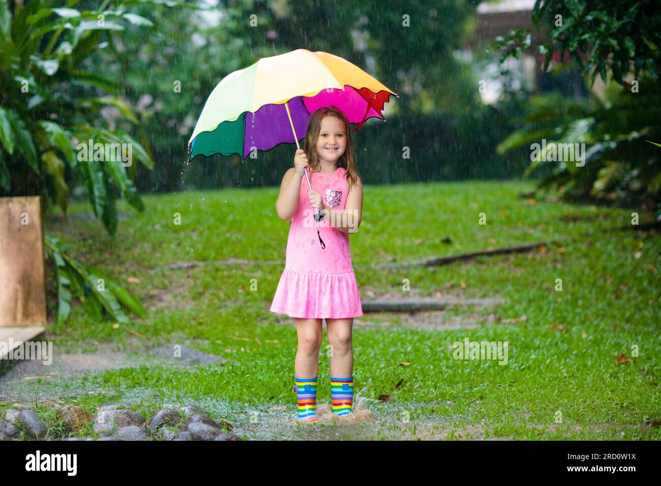 Kid playing out in the rain. Children with umbrella and rain boots play