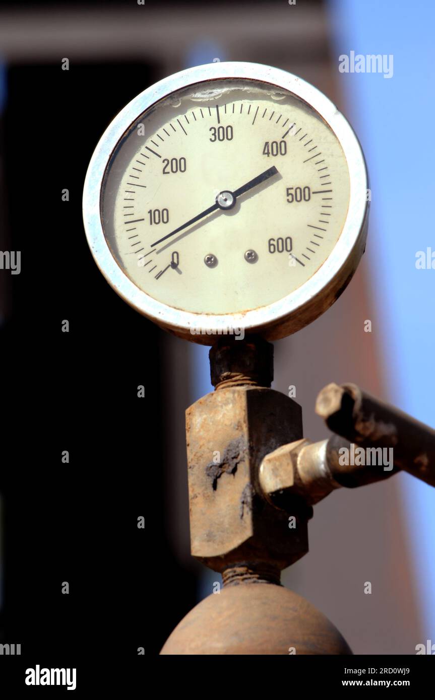 Gauge measures the PSI on an oil derrick. It is weathered and rusty and ...