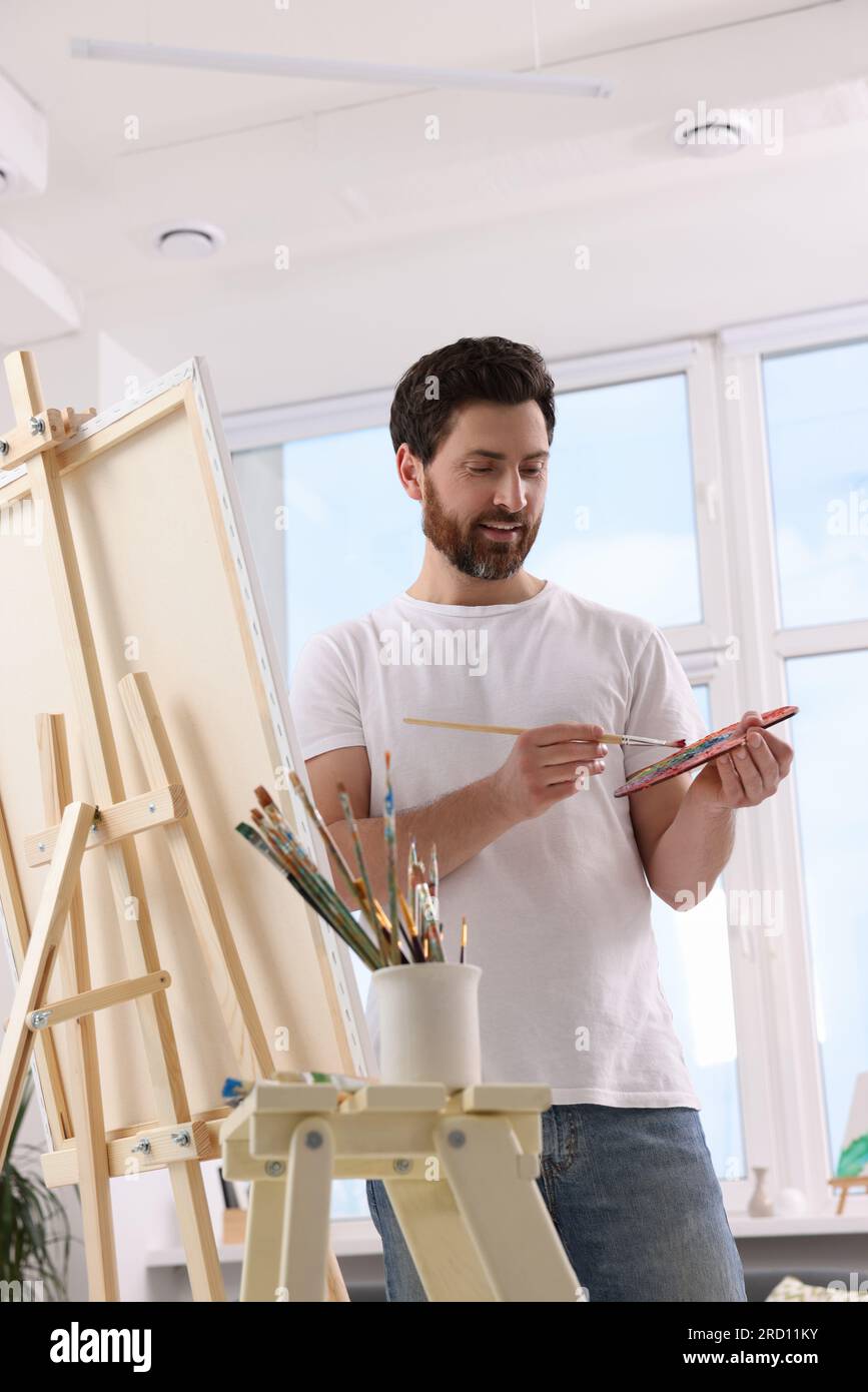Man painting in studio. Using easel to hold canvas Stock Photo - Alamy