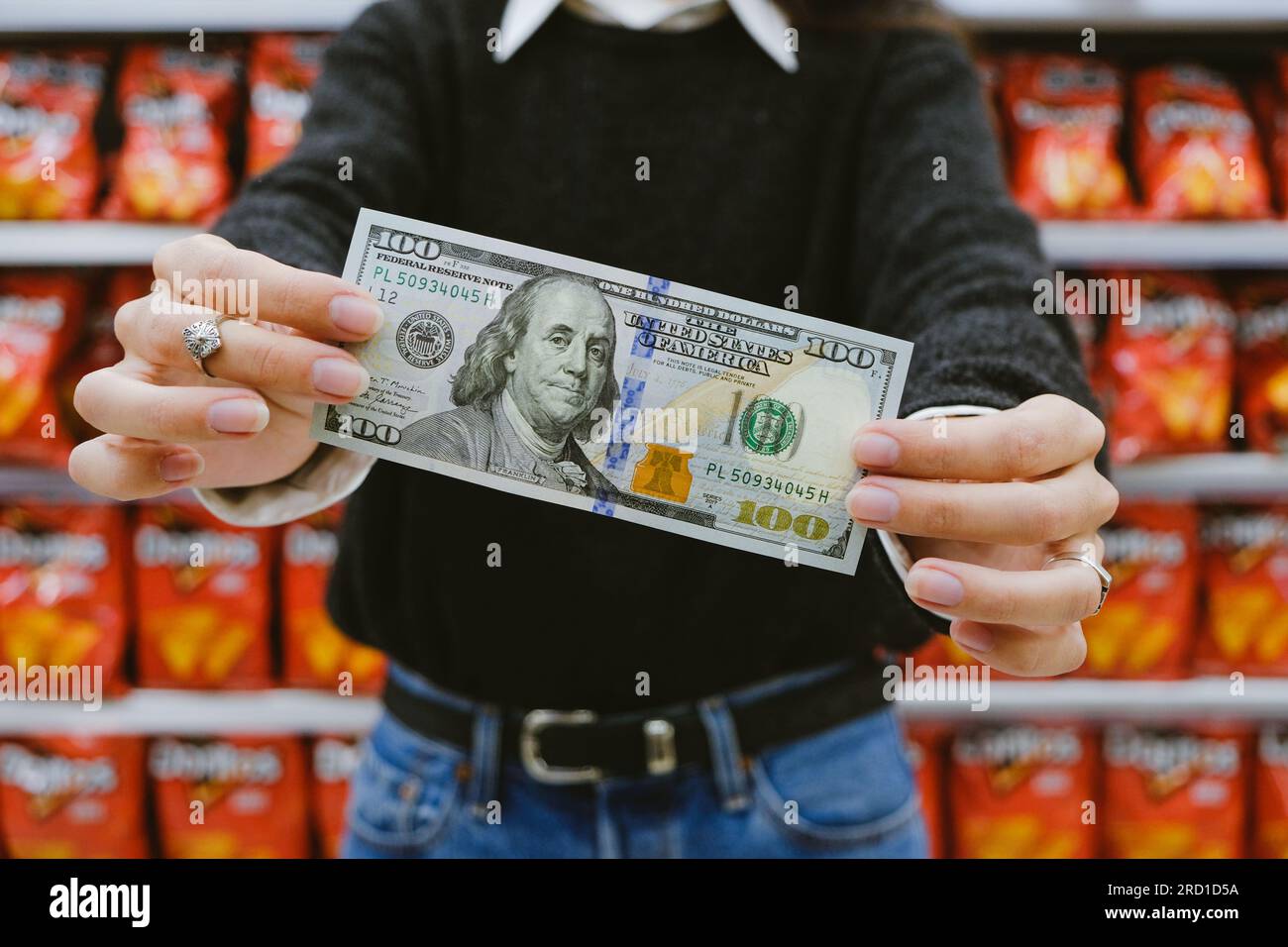Woman Holding A 100 Dollar Bill In The Supermarket. Concept Of Inflation And Rise Of The Dollar In Argentina Stock Photo