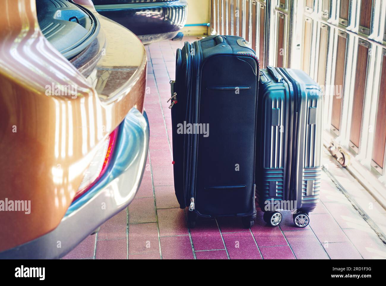 Two luggage stand on the floor close to the rear car in a parking lot at home, the concept for road trips. Black luggage with wheels, big size and sma Stock Photo
