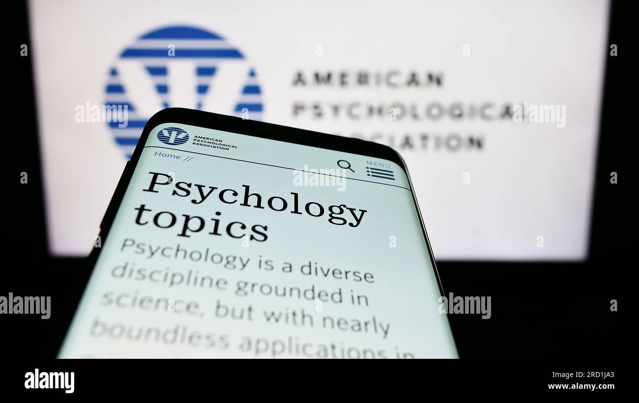 Mobile phone with website of American Psychological Association (APA) on screen in front of logo. Focus on top-left of phone display. Stock Photo