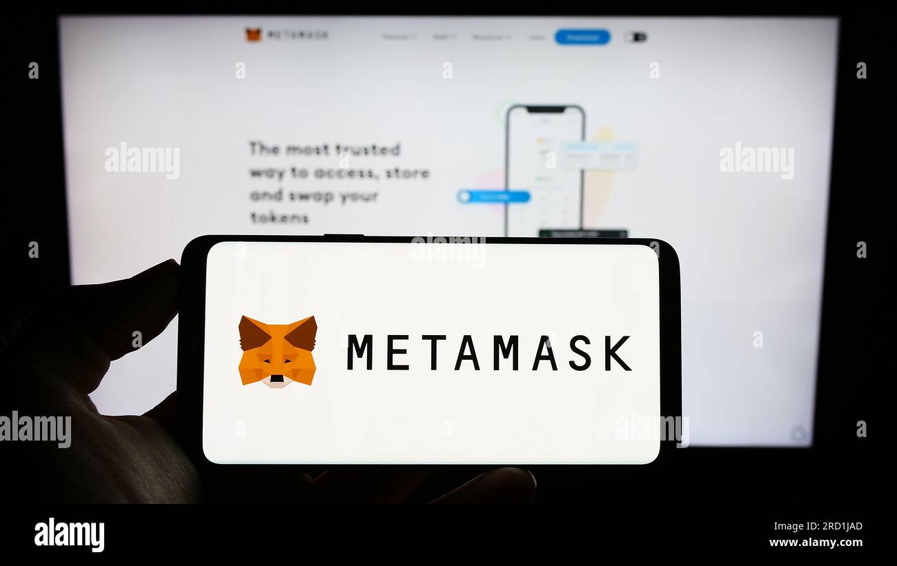 Person holding cellphone with logo of cryptocurrency wallet software  MetaMask on screen in front of business webpage. Focus on phone display  Stock Photo - Alamy