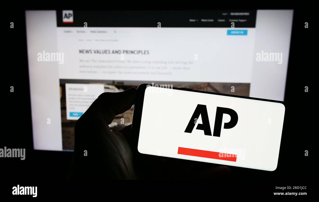 Person holding mobile phone with logo of American news agency Associated Press (AP) on screen in front of web page. Focus on phone display. Stock Photo