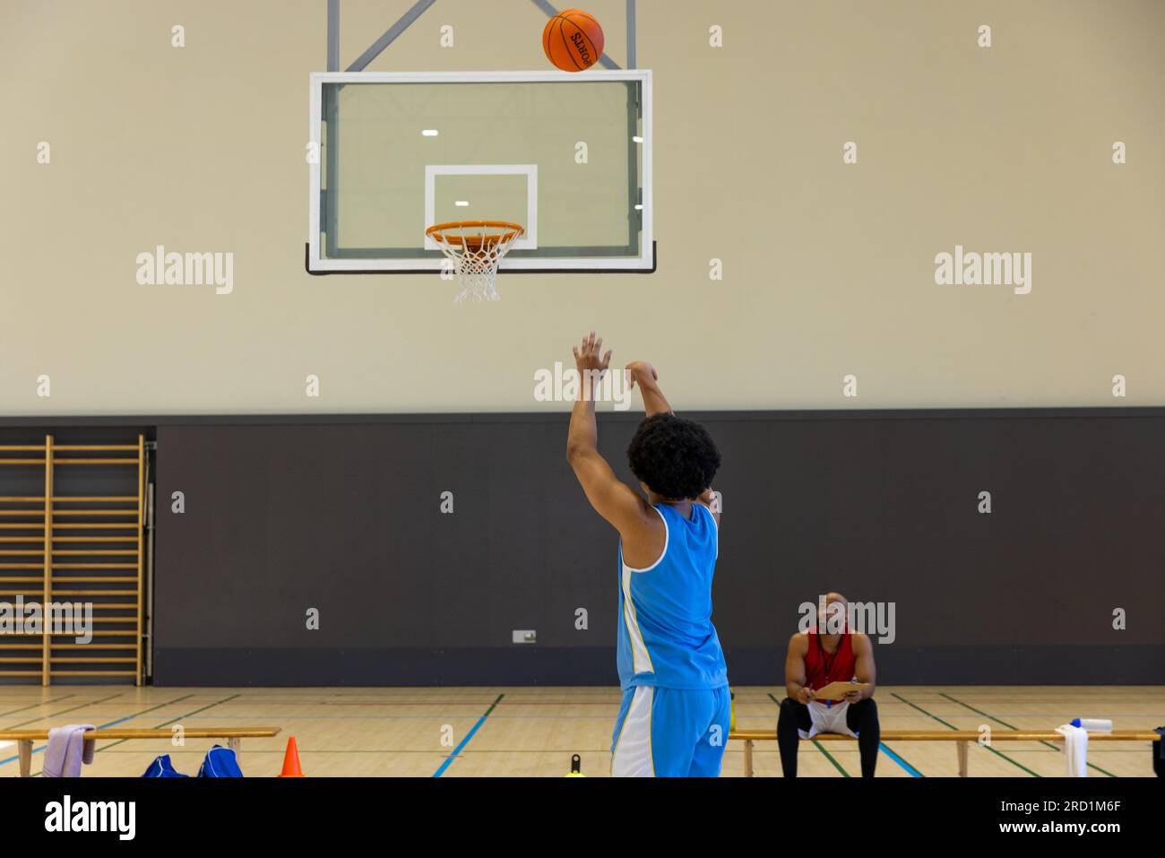 Biracial male basketball player shooting basketball with coach on bench