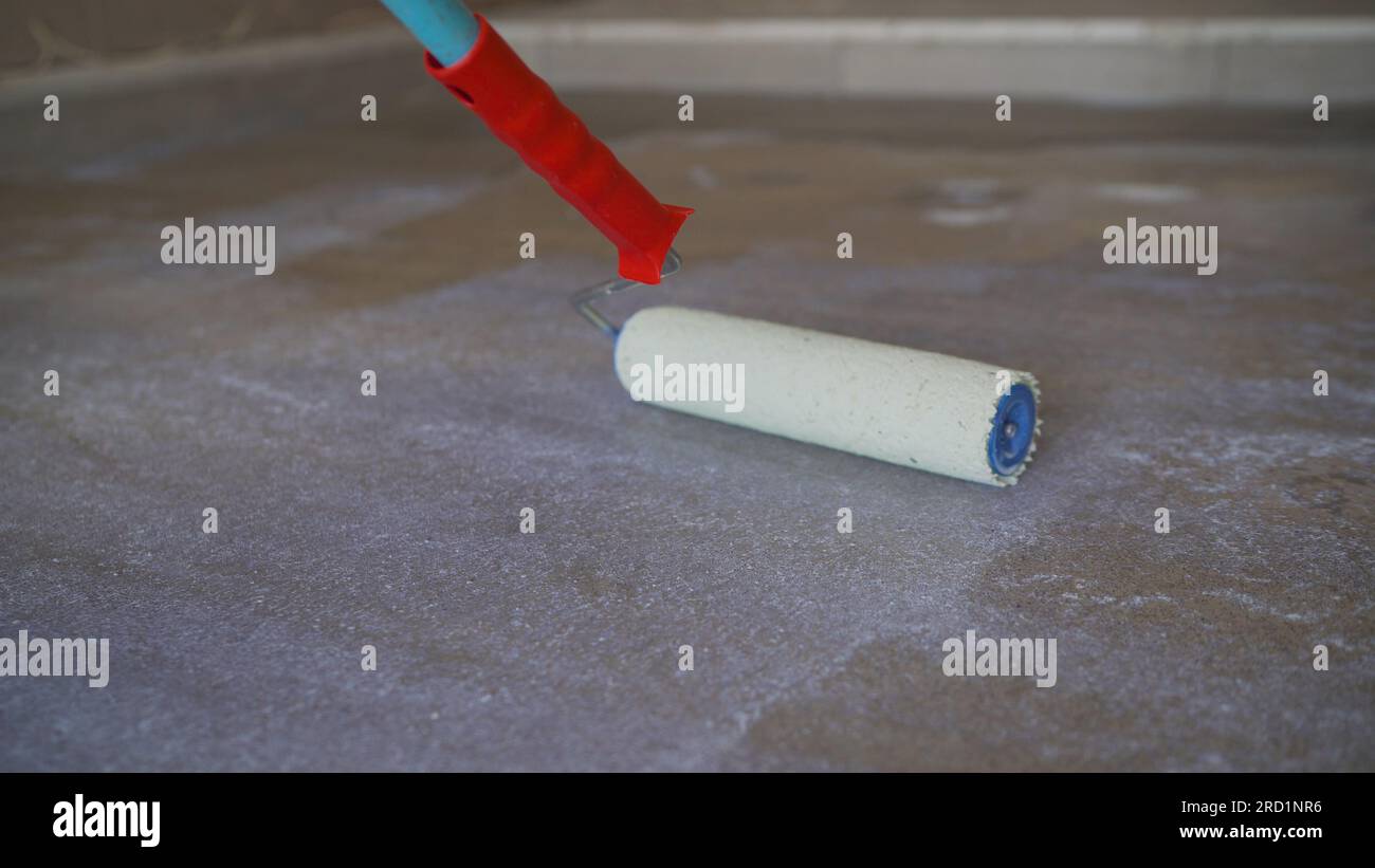 A worker applies the primer to the concrete floor with a roller