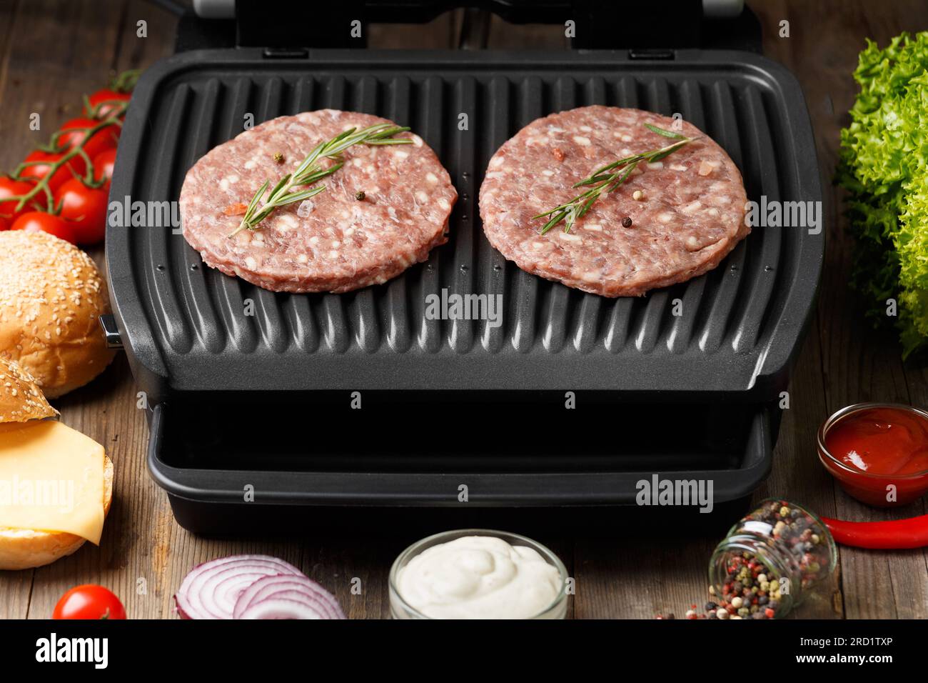 Beef patties for a burger are fried on a smart electric grill on a rustic wooden background