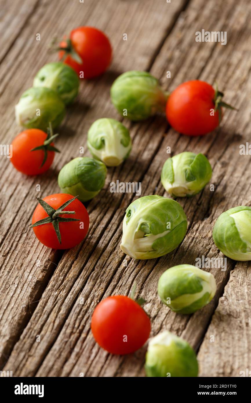 Cherry tomatoes and Brussels sprouts on an aged wooden background. Mix of fresh healthy vegetables. The concept of proper, wholesome nutrition. Stock Photo