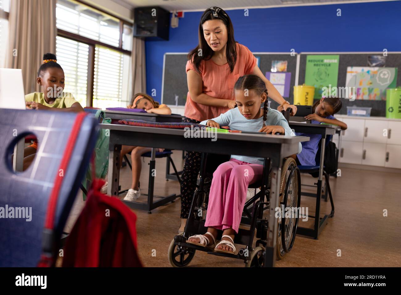 Diverse female teacher and schoolgirl in wheelchair in elementary