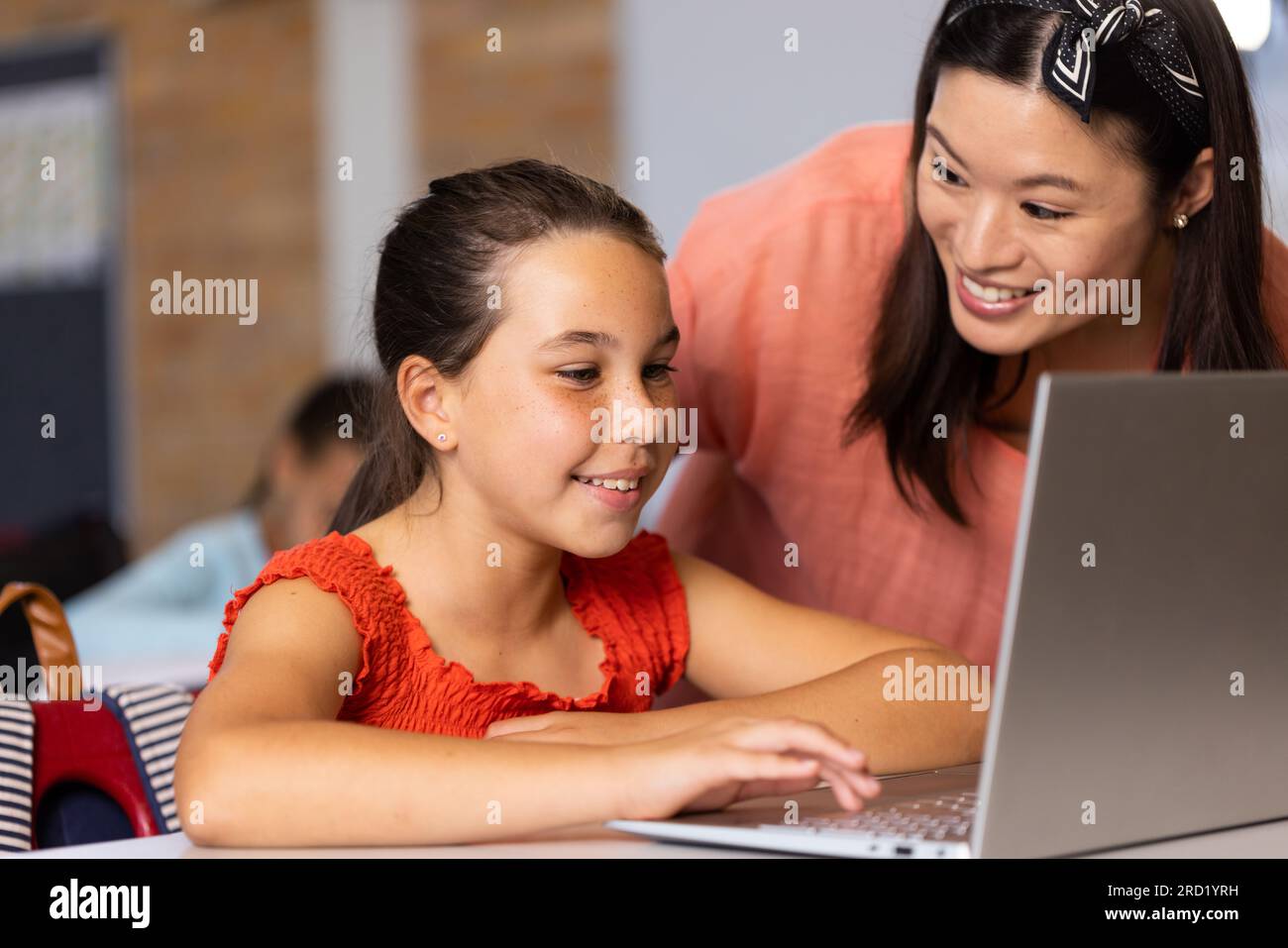Diverse female teacher and schoolgirl using laptop in elementary school ...