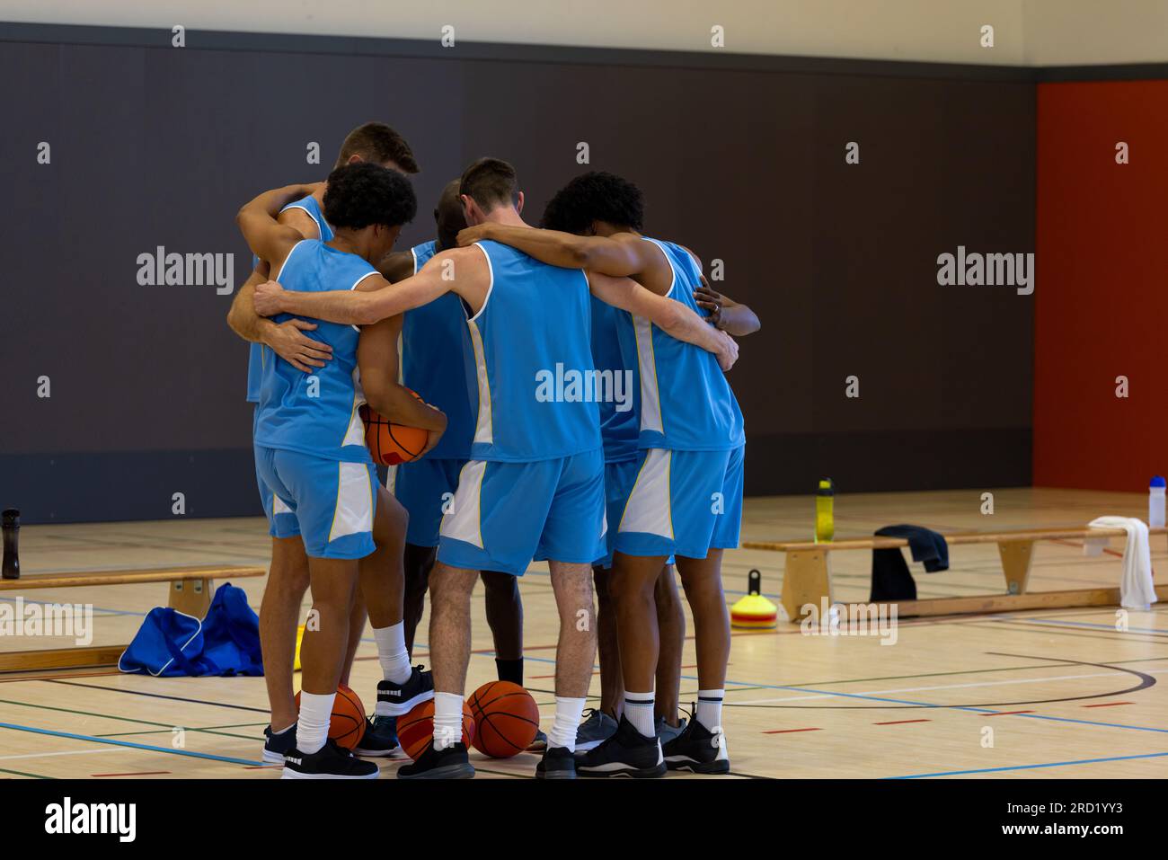 Diverse male basketball players embracing and holding basketball at gym Stock Photo