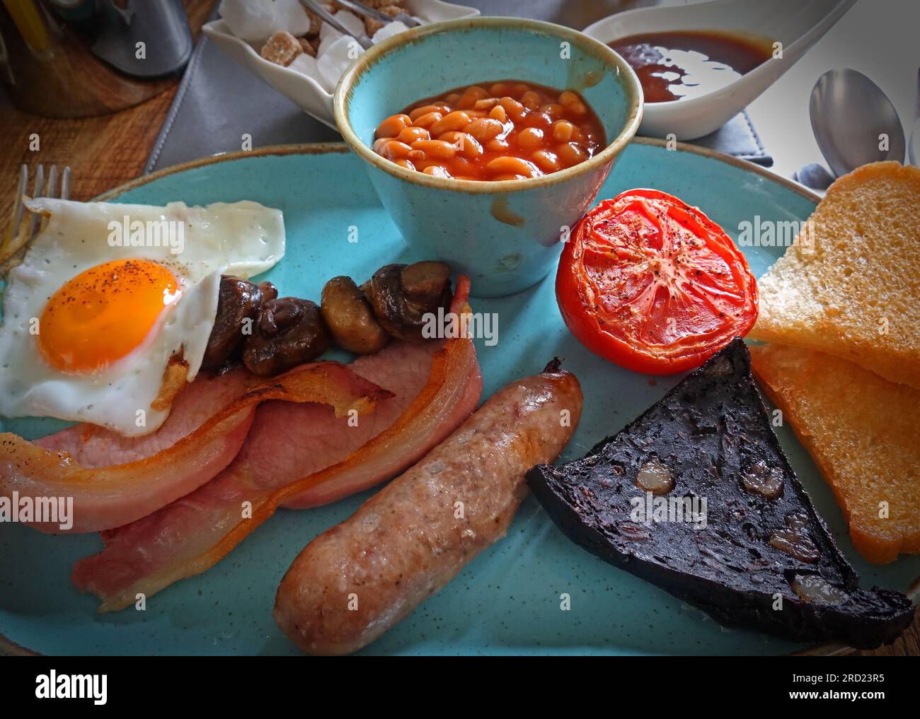 British traditional cooked breakfast, fried egg, bacon, sausage, black pudding, fried bread, beans, grilled tomato and mushrooms Stock Photo