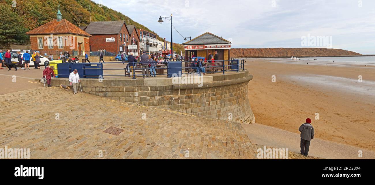 A lone man stands on the beach at Filey seafront beneath the promenade, with the wide sandy shoreline stretching along the North Yorkshire coast Stock Photo