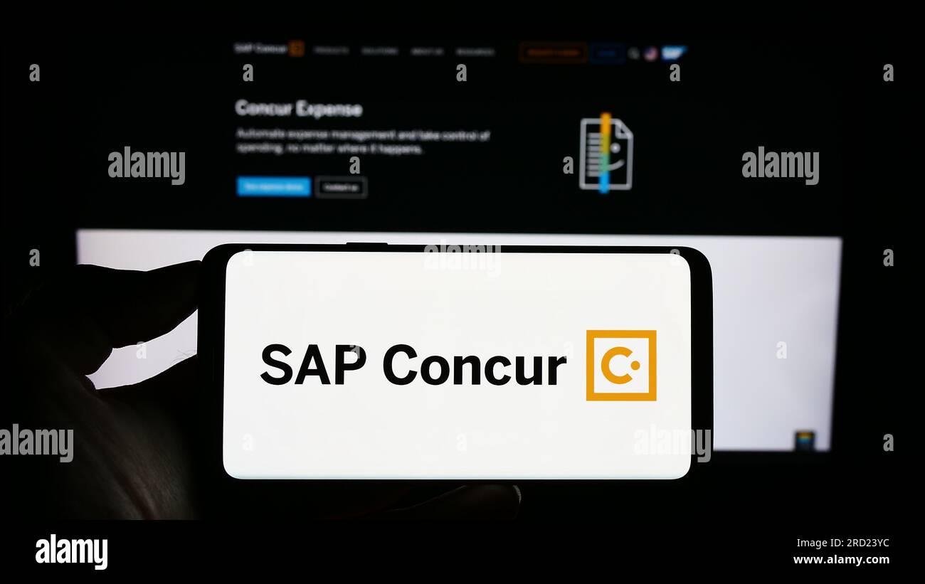 Person holding cellphone with logo of expense management software SAP Concur on screen in front of business webpage. Focus on phone display. Stock Photo