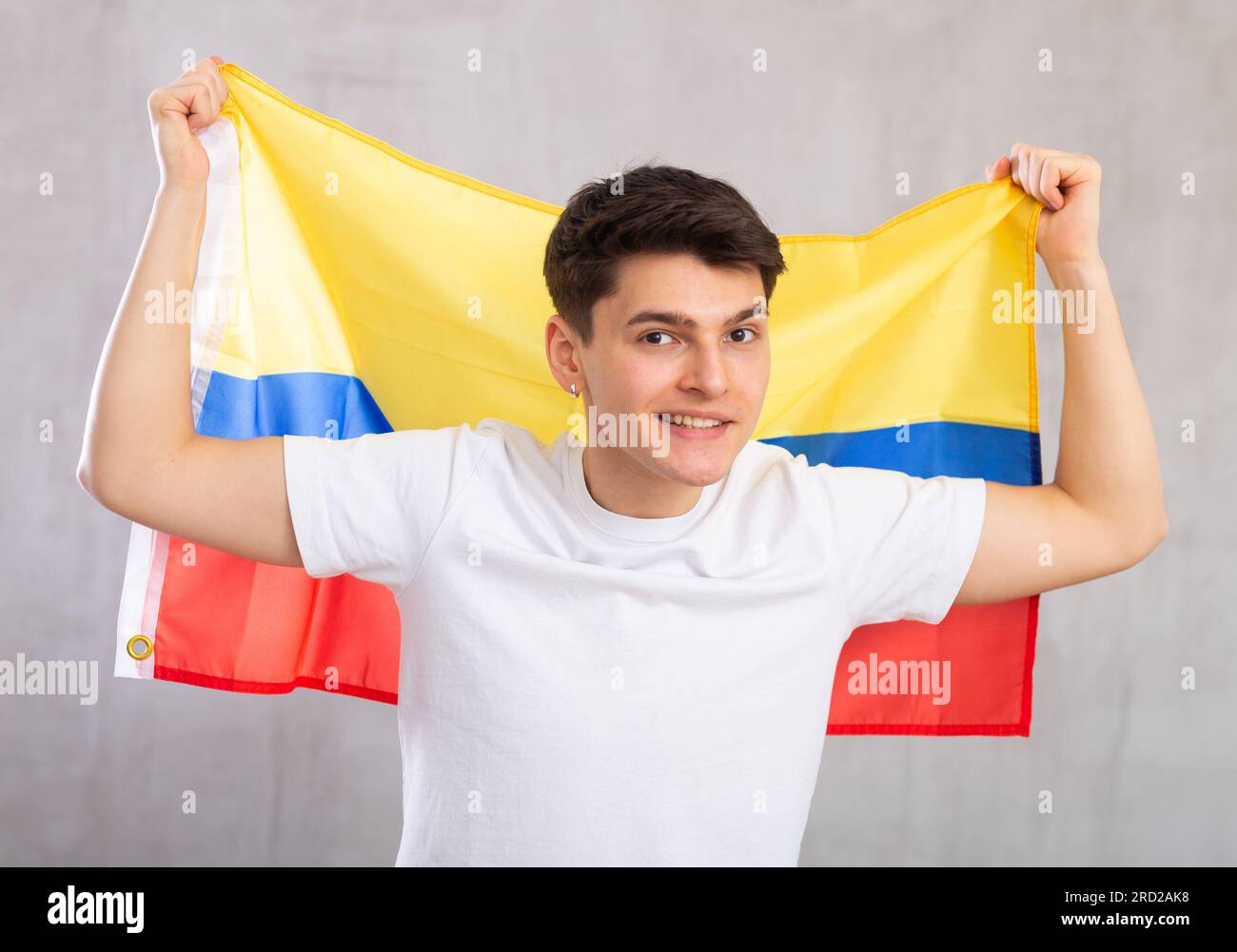 Man in holds unfurled flag of Colombia in hands raised above head against gray wall Stock Photo