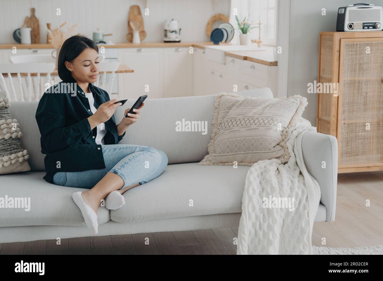 Woman check bank account via mobile app, sitting on couch at home