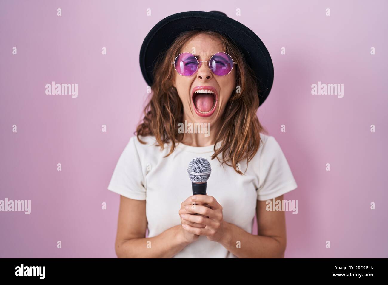 Beautiful brunette woman singing song using microphone angry and mad ...