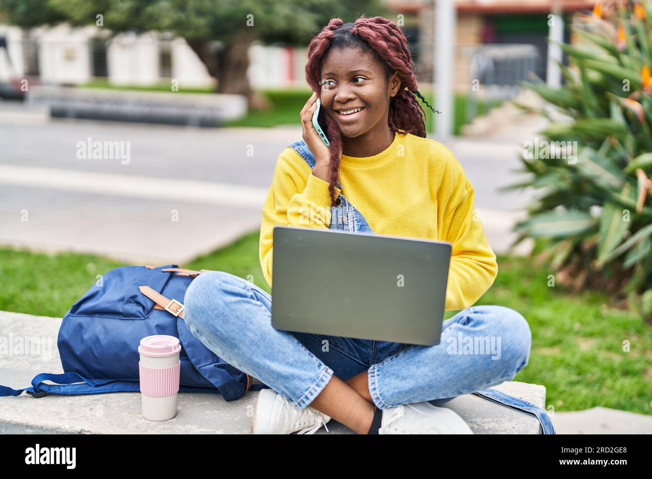 African american woman student using laptop talking on smartphone at ...