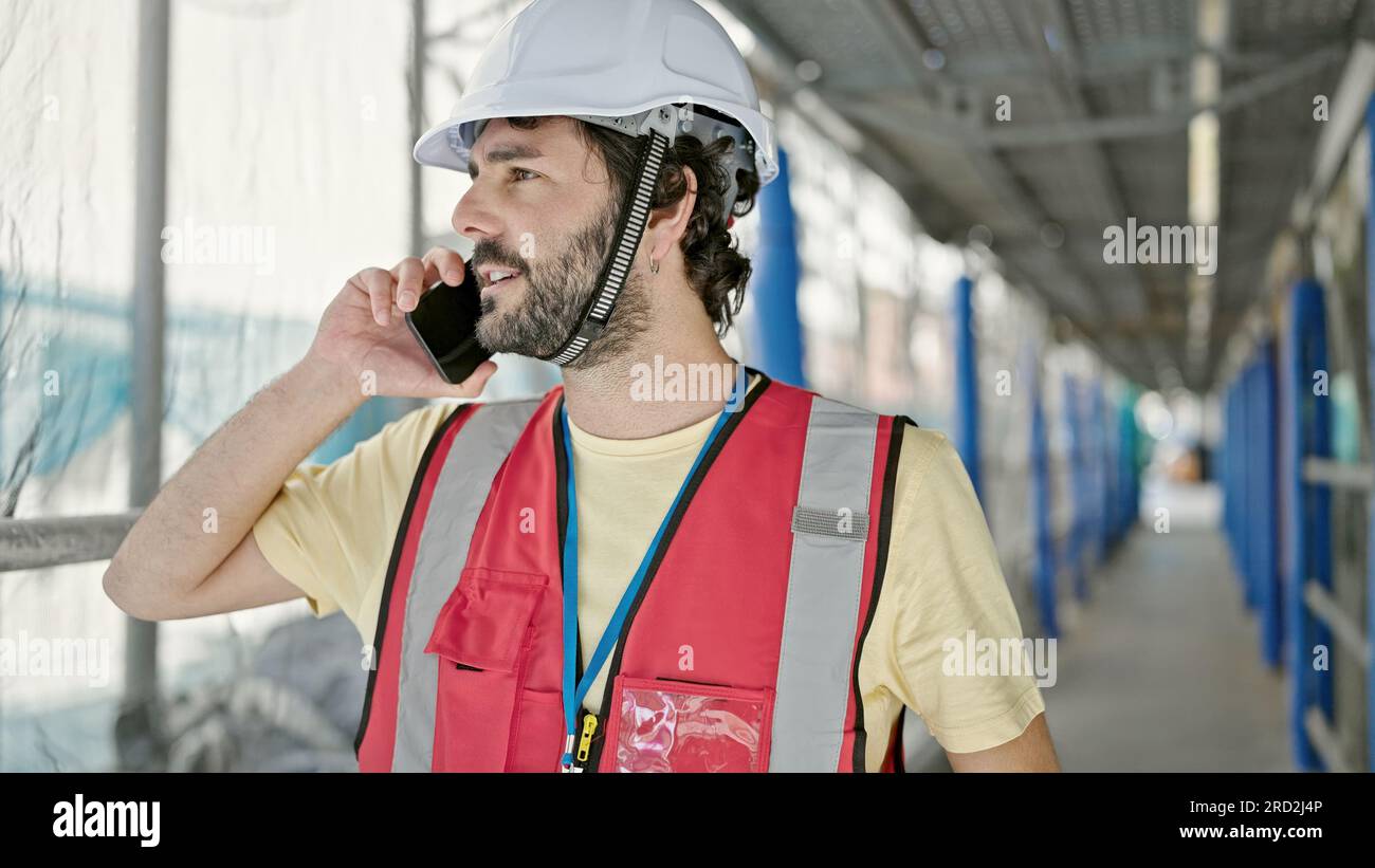 Young hispanic man builder talking on smartphone standing at street Stock Photo