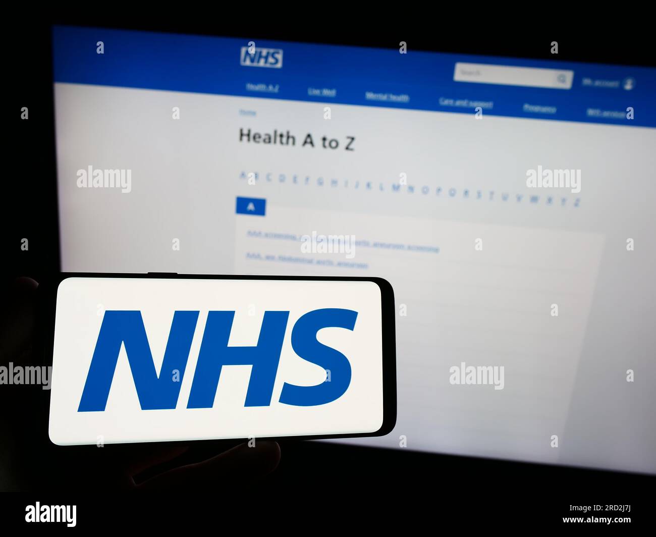 Person holding smartphone with logo of British National Health Service (NHS) on screen in front of website. Focus on phone display. Stock Photo