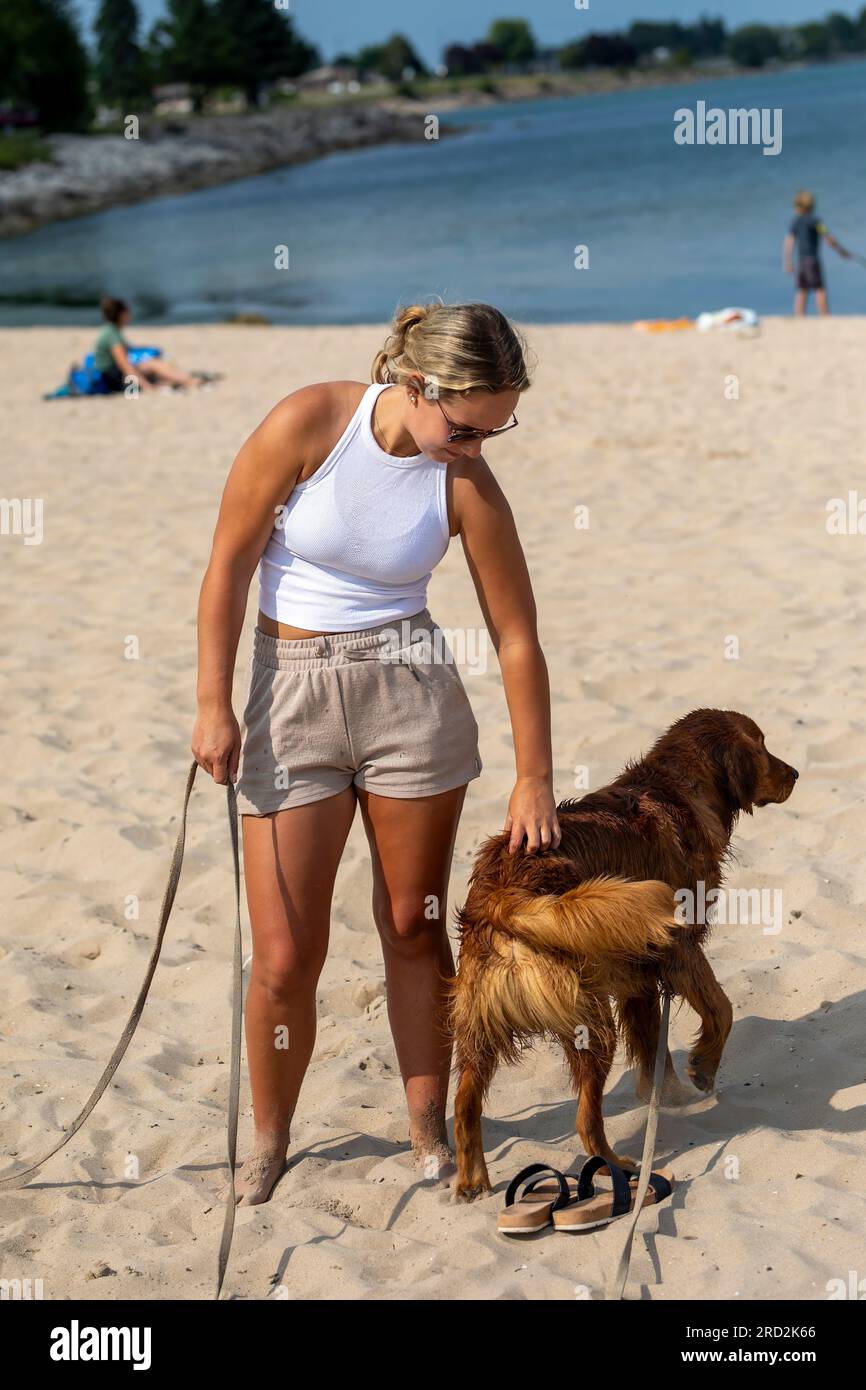 Manitowoc, WI USA July 16 2023: beautiful young miss playing with dog on lake Michigan beach Stock Photo