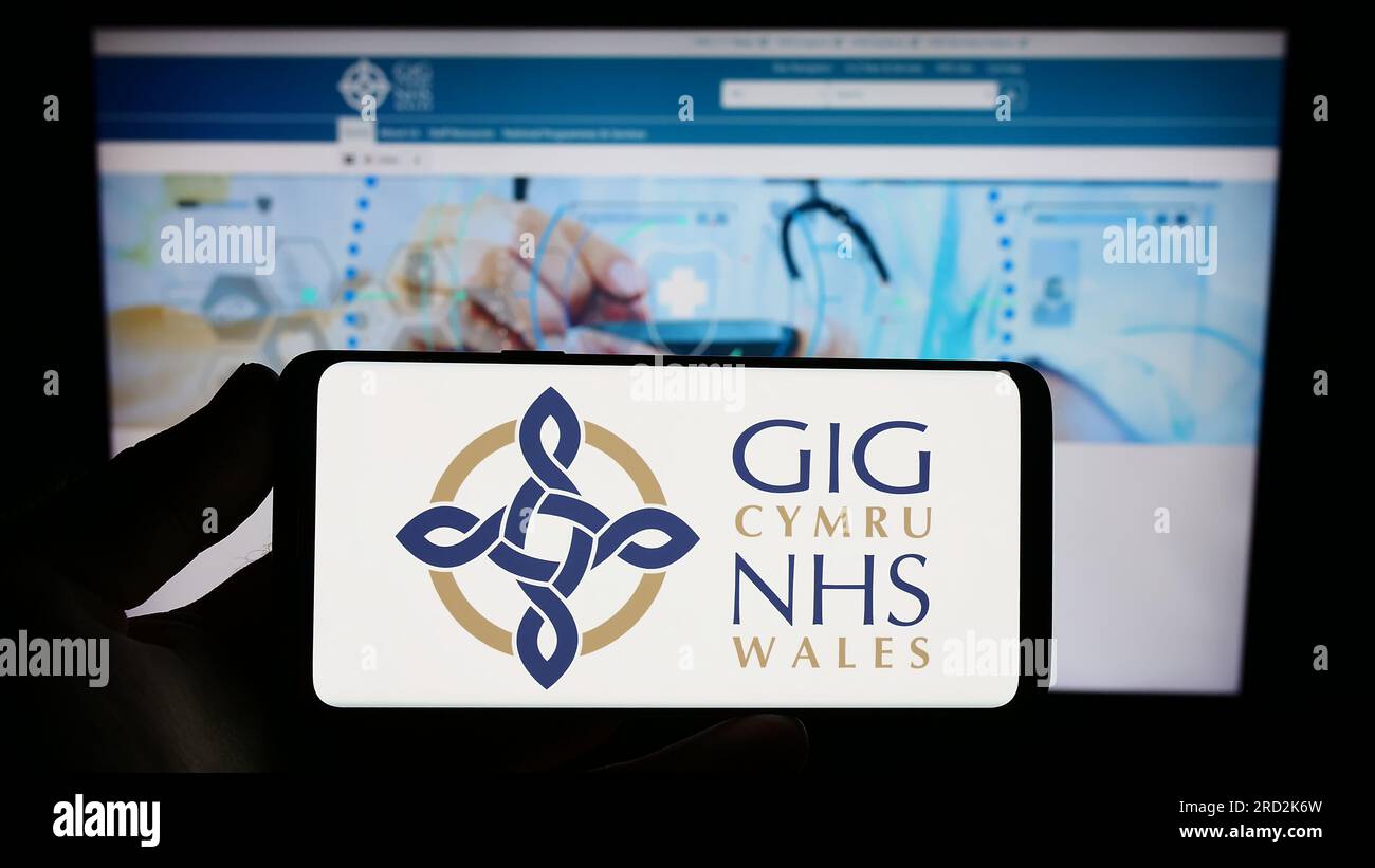Person holding smartphone with logo of British healthcare system NHS Wales on screen in front of website. Focus on phone display. Stock Photo