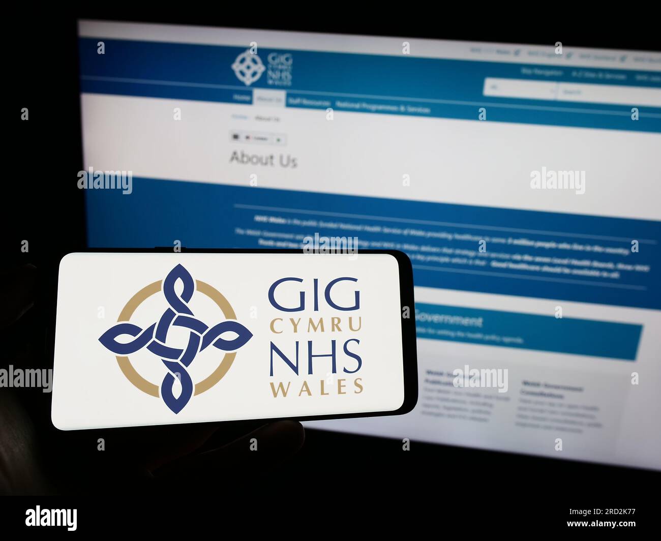 Person holding mobile phone with logo of British healthcare system NHS Wales on screen in front of web page. Focus on phone display. Stock Photo
