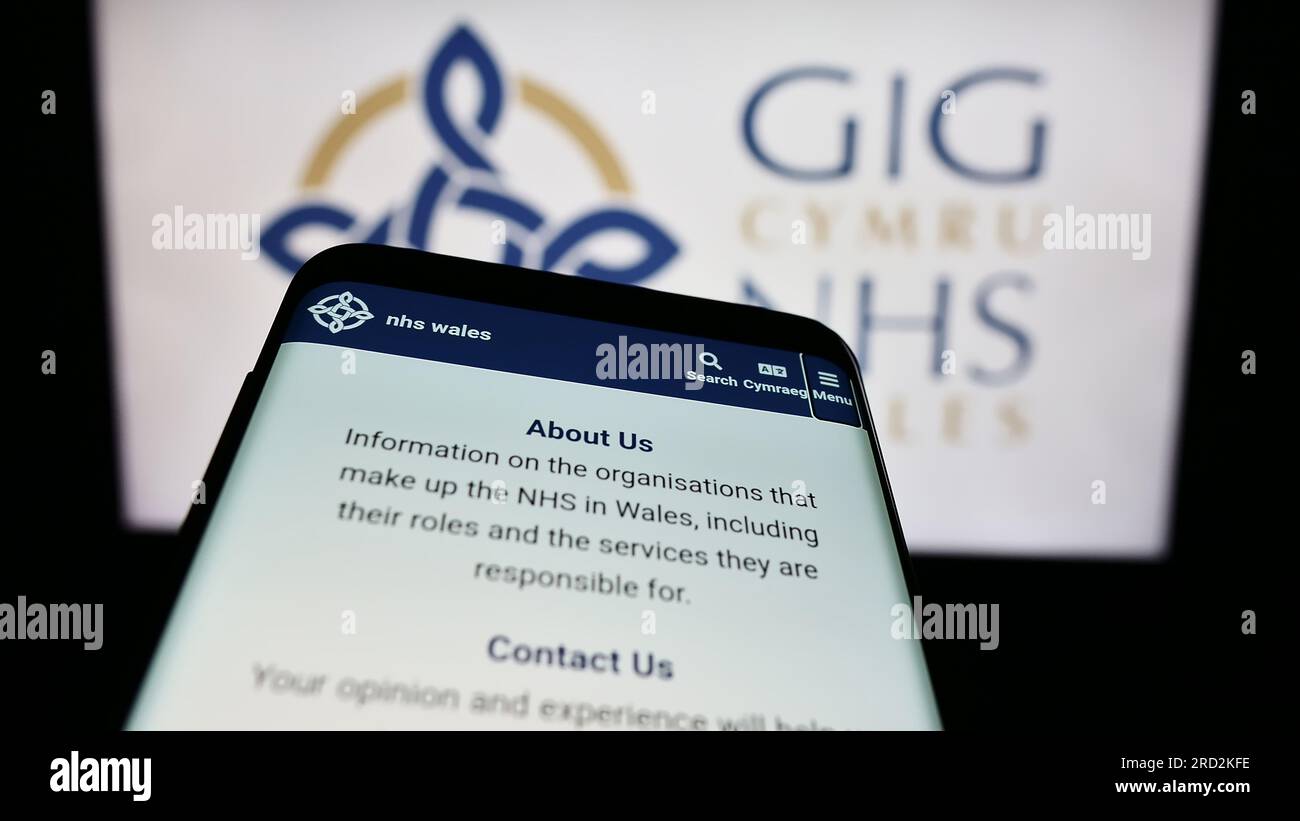 Smartphone with website of British healthcare system NHS Wales on screen in front of logo. Focus on top-left of phone display. Stock Photo