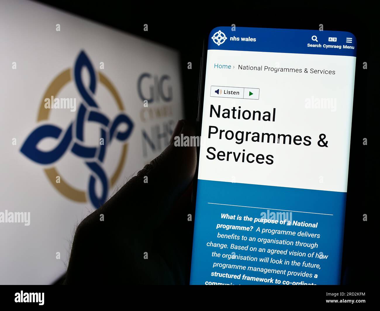 Person holding cellphone with webpage of British healthcare system NHS Wales on screen in front of logo. Focus on center of phone display. Stock Photo