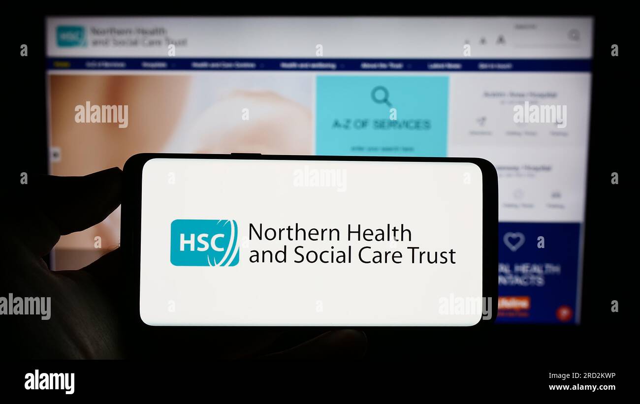 Person holding cellphone with logo of Health and Social Care (HSC) in Northern Ireland on screen in front of webpage. Focus on phone display. Stock Photo