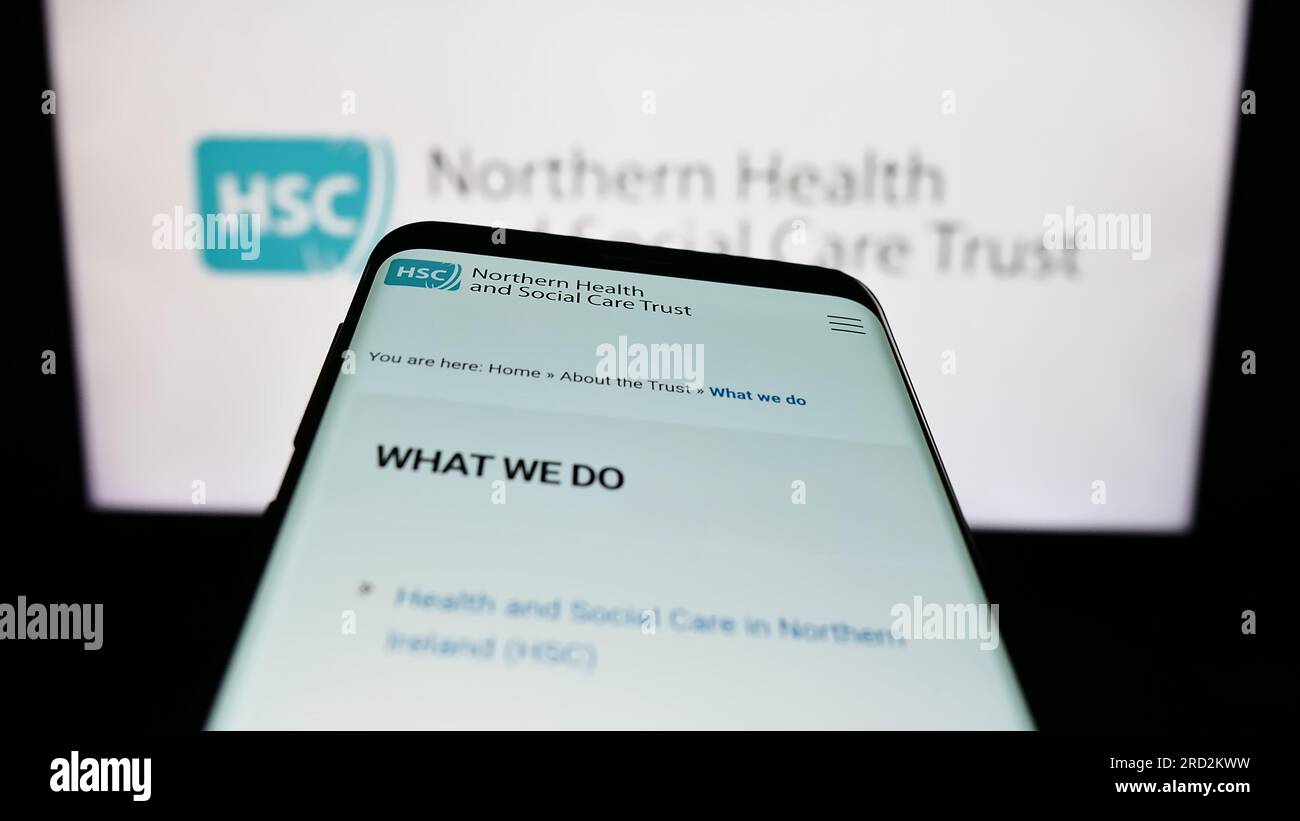 Mobile phone with website of Health and Social Care (HSC) in Northern Ireland on screen in front of logo. Focus on top-left of phone display. Stock Photo