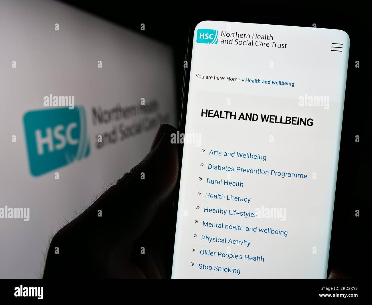 Person holding smartphone with webpage of Health and Social Care (HSC) in Northern Ireland on screen with logo. Focus on center of phone display. Stock Photo